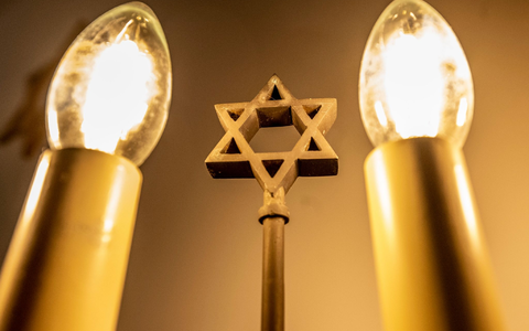 Ein siebenarmiger Leuchter (Menora) mit einem Davidstern in der Mitte leuchtet in einer Synagoge. Fragen zum Judentum werden auf einer Website beantwortet. - Foto: David Inderlied/dpa