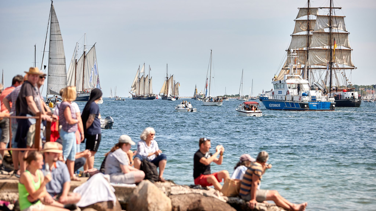 Menschen verfolgen an der Förde die Windjammerparade. - Foto: Georg Wendt/dpa