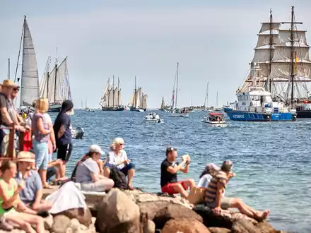 Menschen verfolgen an der Förde die Windjammerparade. - Foto: Georg Wendt/dpa