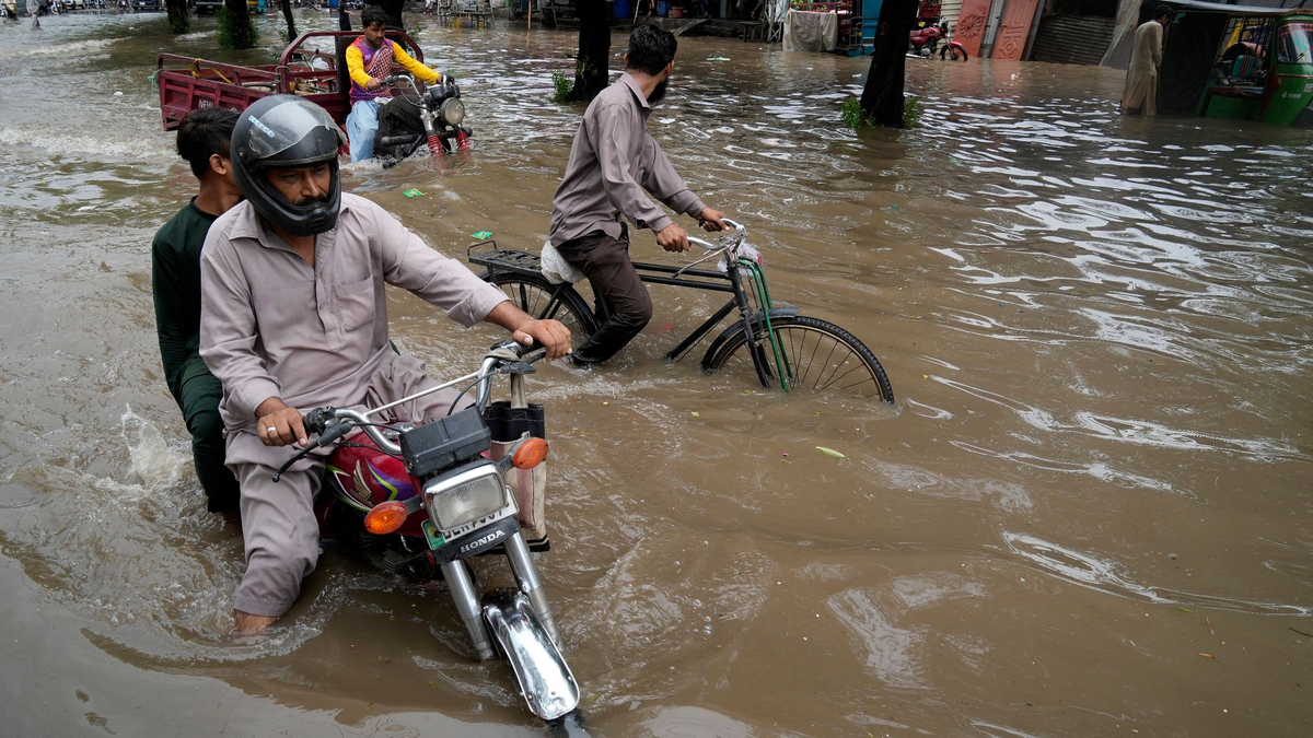 Motorradfahrer auf einer überschwemmten Straße im pakistanischen Lahore. - Foto: K.M. Chaudary/AP/dpa