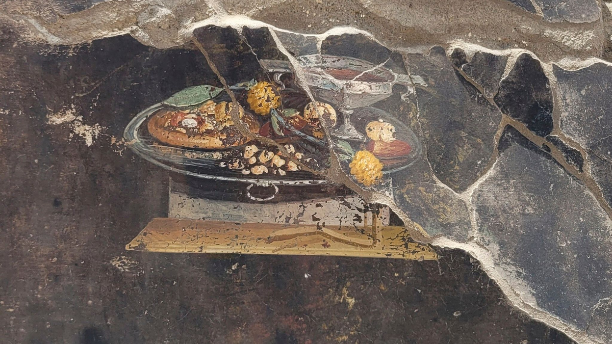 Die Wand eines pompejanischen Hauses mit einem Fresko, das einen Tisch mit Speisen darstellt, darunter auch eine Art Pizza. - Foto: ---/Pompeii Archaelogical Park/AP/dpa