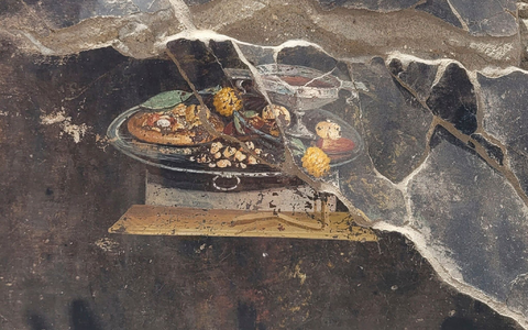 Die Wand eines pompejanischen Hauses mit einem Fresko, das einen Tisch mit Speisen darstellt, darunter auch eine Art Pizza. - Foto: ---/Pompeii Archaelogical Park/AP/dpa