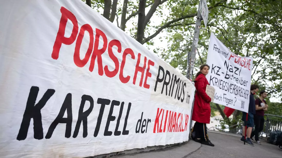 Demonstranten mit Plakaten vor Beginn der Porsche-Hauptversammlung in Stuttgart. - Bild: Marijan Murat/dpa
