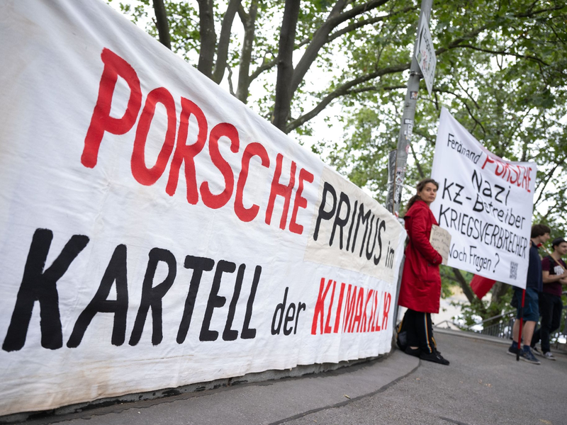 Demonstranten mit Plakaten vor Beginn der Porsche-Hauptversammlung in Stuttgart. - Foto: Marijan Murat/dpa
