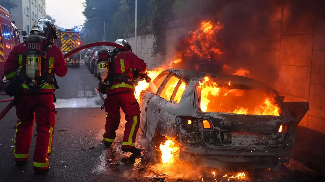 Feuerwehrleute löschen ein brennendes Auto am Rande der Ausschreitungen westlich von Paris. - Bild: Zakaria Abdelkafi/AFP/dpa