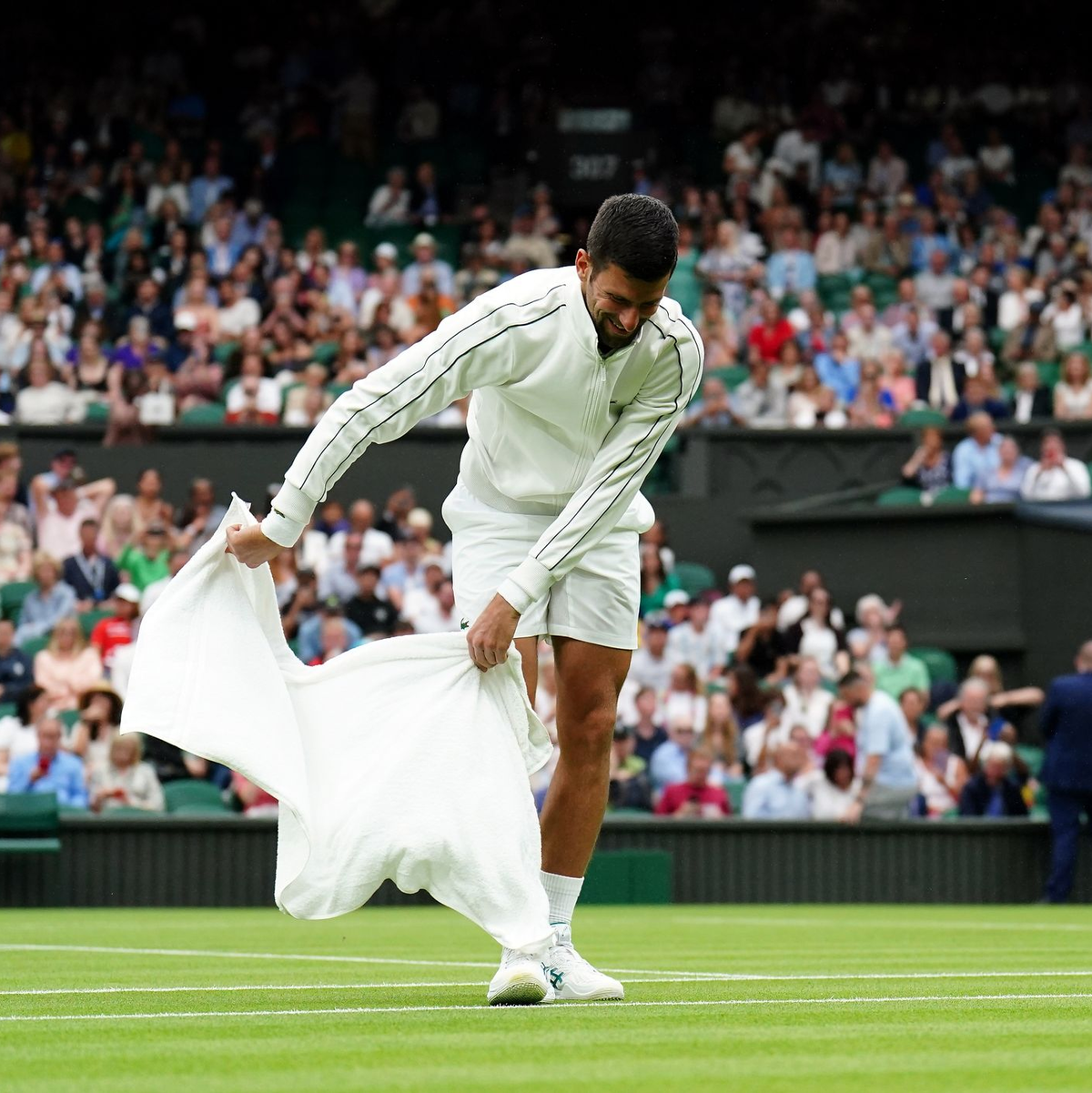 Novak Djokovic trocknet während der Regenunterbrechung den Rasen. - Foto: Zac Goodwin/PA Wire/dpa