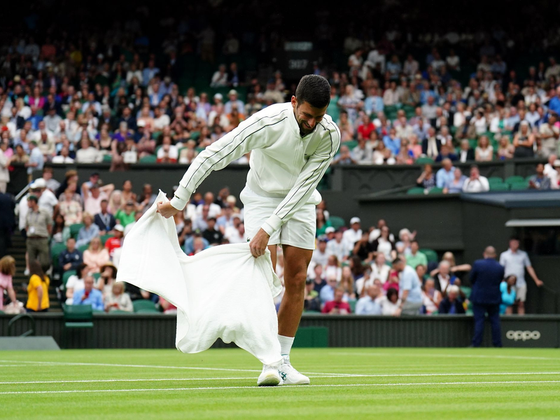 Novak Djokovic trocknet während der Regenunterbrechung den Rasen. - Foto: Zac Goodwin/PA Wire/dpa