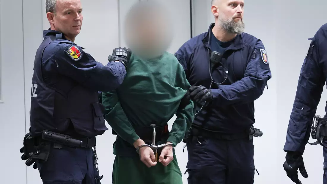 Der Angeklagte Ibrahim A. wird von Justizbeamten an seinen Platz im Gerichtssaal gebracht. - Bild: Christian Charisius/dpa