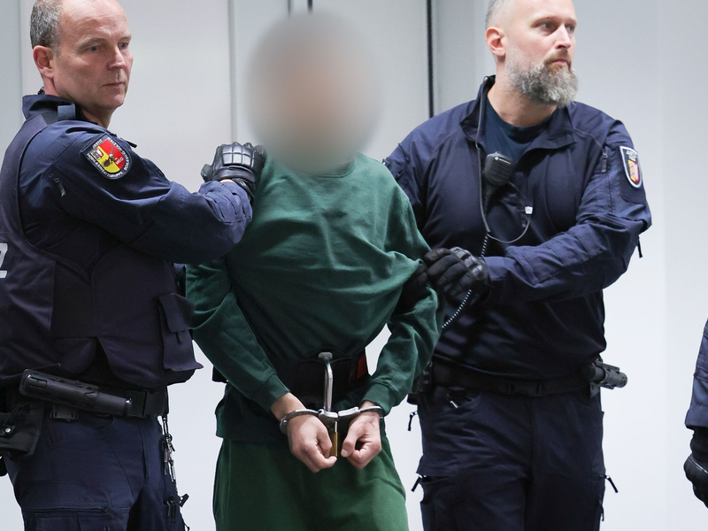 Der Angeklagte Ibrahim A. wird von Justizbeamten an seinen Platz im Gerichtssaal gebracht. - Foto: Christian Charisius/dpa
