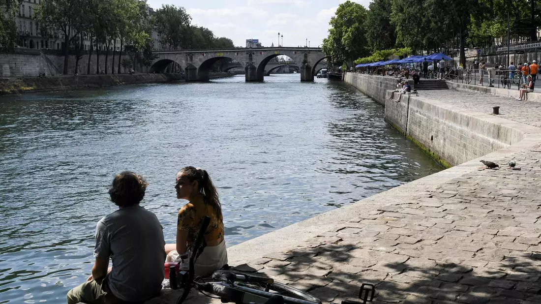 Zwei junge Leute sitzen am Ufer der Seine in Paris. - Bild: Alain Jocard/AFP/dpa