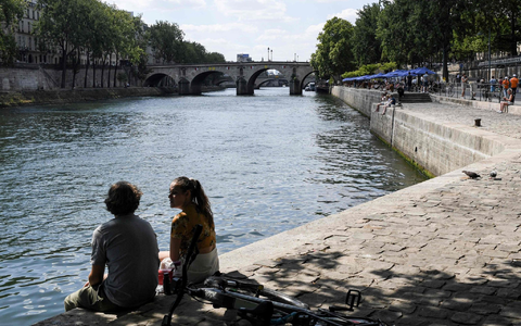 Zwei junge Leute sitzen am Ufer der Seine in Paris. - Foto: Alain Jocard/AFP/dpa