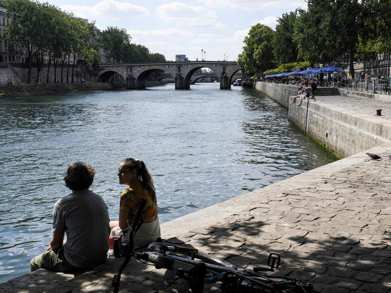 Zwei junge Leute sitzen am Ufer der Seine in Paris. - Foto: Alain Jocard/AFP/dpa