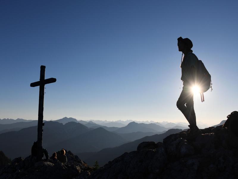 Eine Ausflüglerin genießt den Blick am Gipfelkreuz des Taubensteins. - Foto: Tobias Hase/dpa