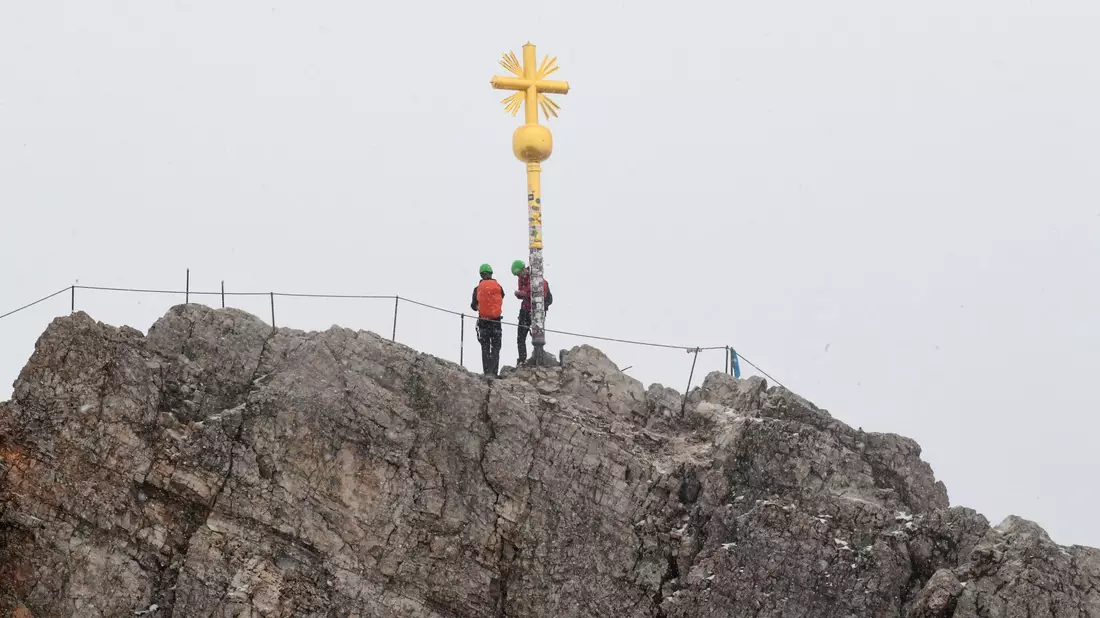 Bergsteiger stehen neben dem Gipfelkreuz des Zugspitzgipfel. - Bild: Felix Hörhager/dpa