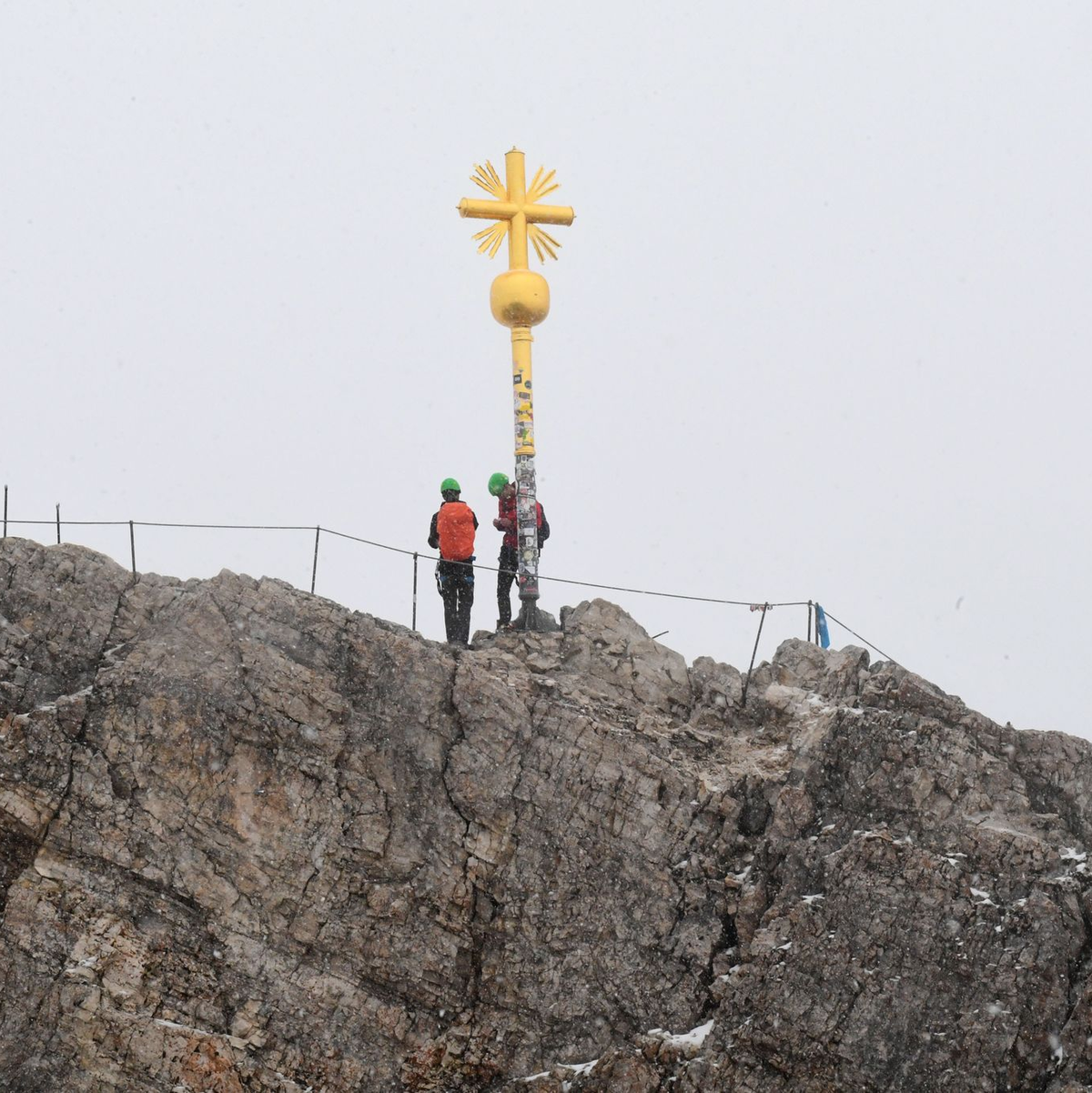 Bergsteiger stehen neben dem Gipfelkreuz des Zugspitzgipfel. - Foto: Felix Hörhager/dpa