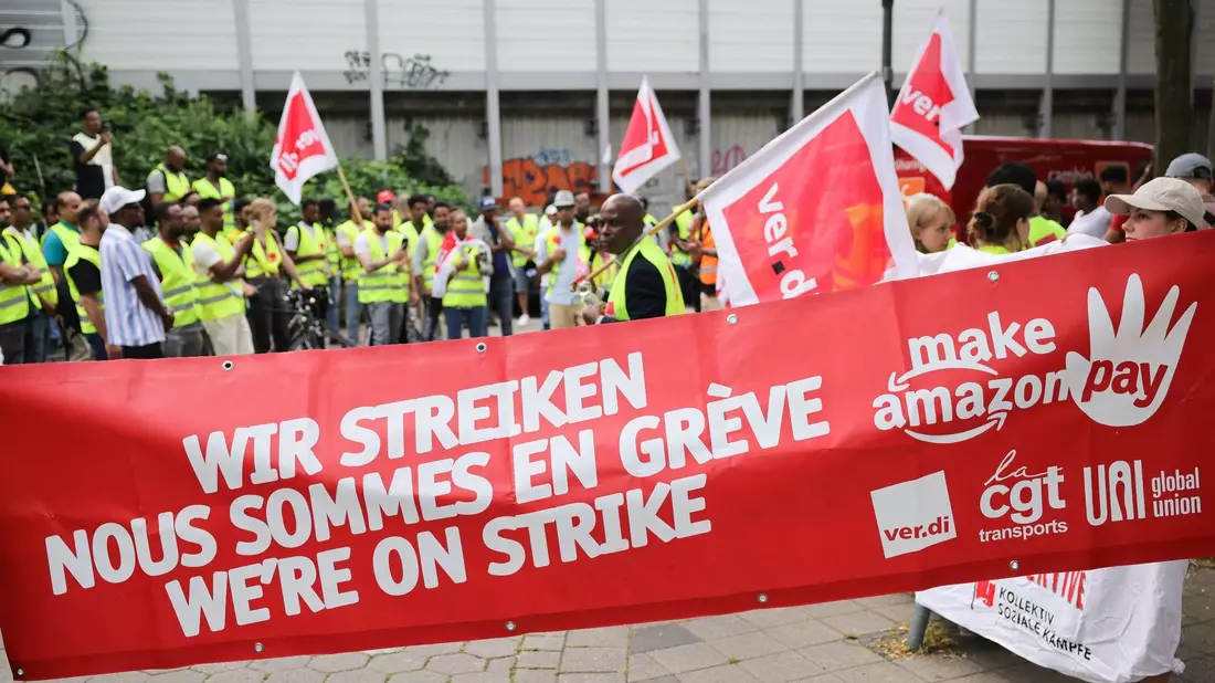 Beschäftigte von Amazon bei einer Demonstration unter dem Titel «Make Amazon Pay! Für gute und gesunde Arbeit bei Amazon!» vor dem Amazon-Verteilzentrum in Hamburg-Veddel. - Bild: Christian Charisius/dpa