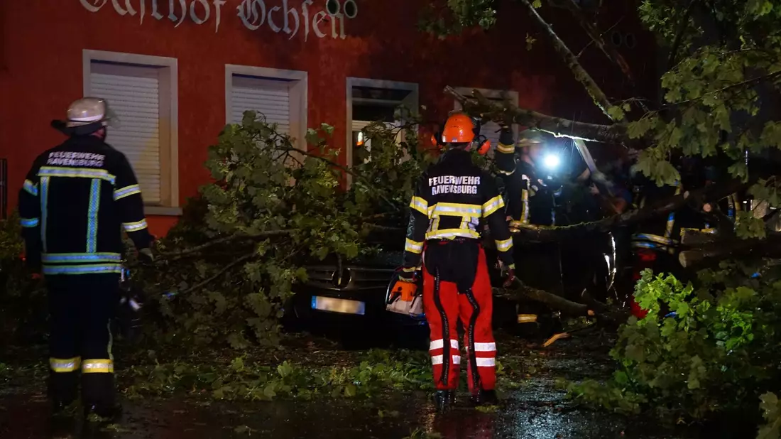 Feuerwehrleute beseitigen einen Baum, der im baden-württembergischen Ravensburg auf ein Auto gestürzt ist. - Bild: David Pichler/dpa