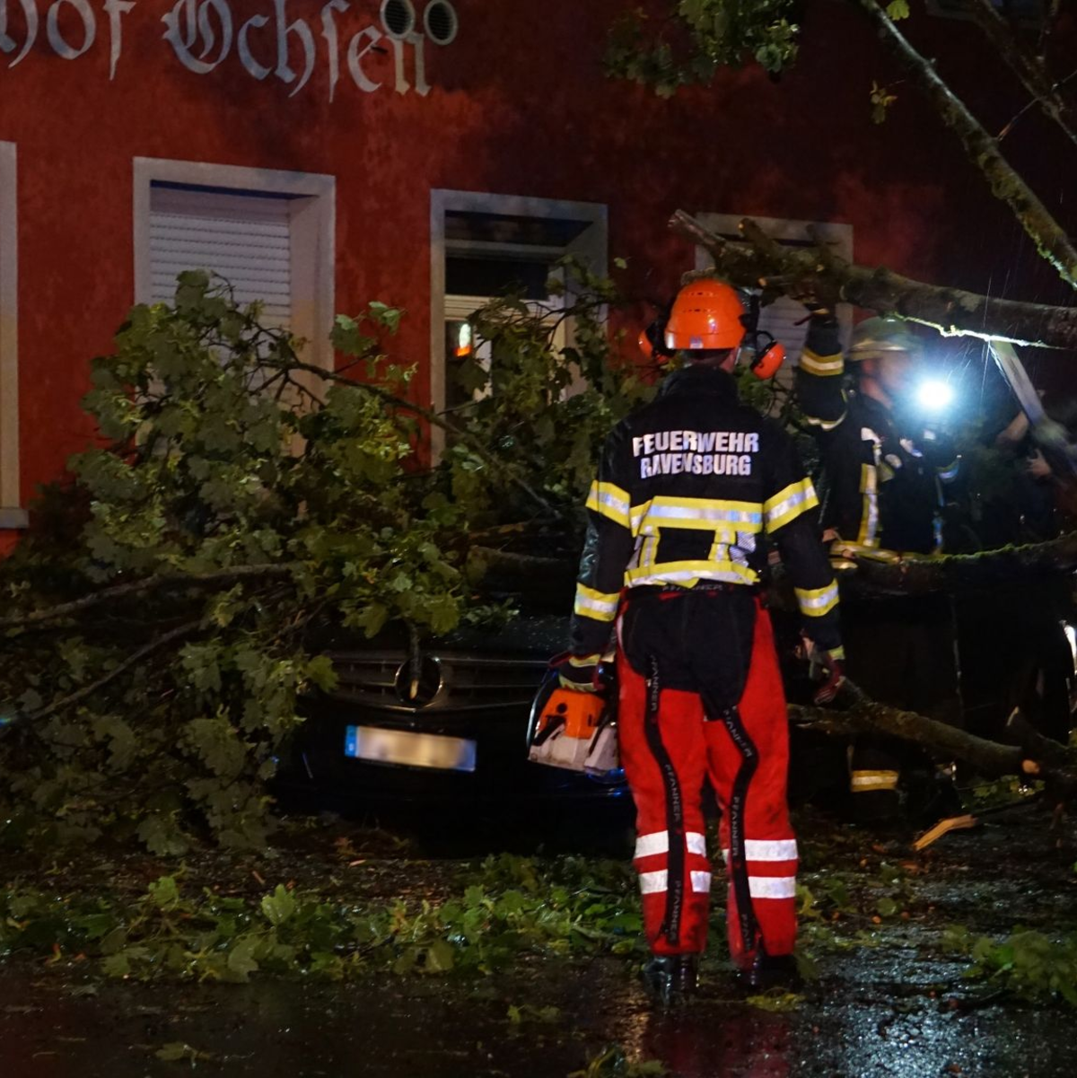 Feuerwehrleute beseitigen einen Baum, der im baden-württembergischen Ravensburg auf ein Auto gestürzt ist. - Foto: David Pichler/dpa
