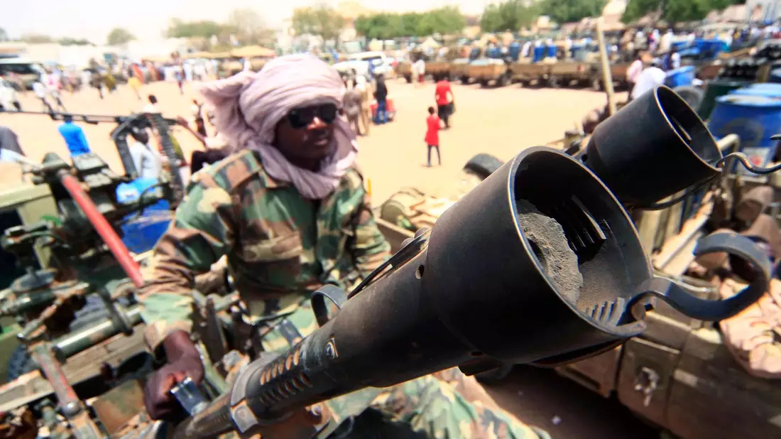 Ein Milizionär sitzt neben militärischer Ausrüstung, die angeblich während eines Gefechts im umkämpften Gebiet in Süd-Darfur erbeutet wurde. - Bild: picture alliance / dpa