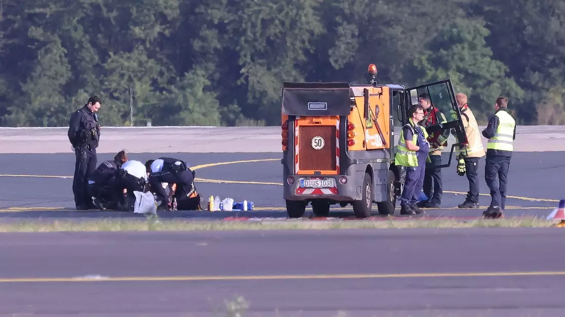 Sicherheitspersonal und Polizisten versuchen am Düsseldofer Flughafen, Aktivisten vom Asphalt auf dem Rollfeld zu lösen. - Bild: David Young/dpa
