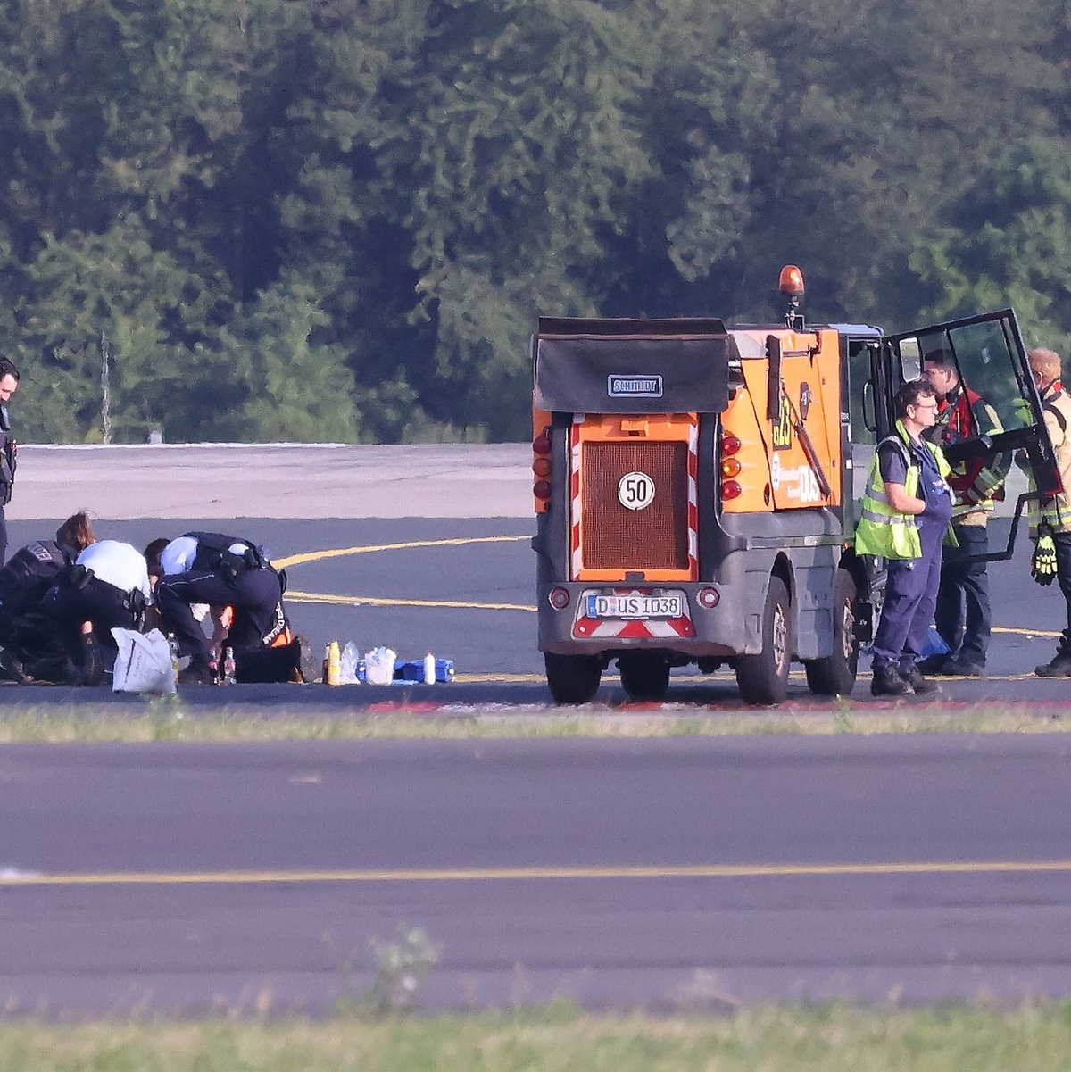Sicherheitspersonal und Polizisten versuchen am Düsseldofer Flughafen, Aktivisten vom Asphalt auf dem Rollfeld zu lösen. - Foto: David Young/dpa