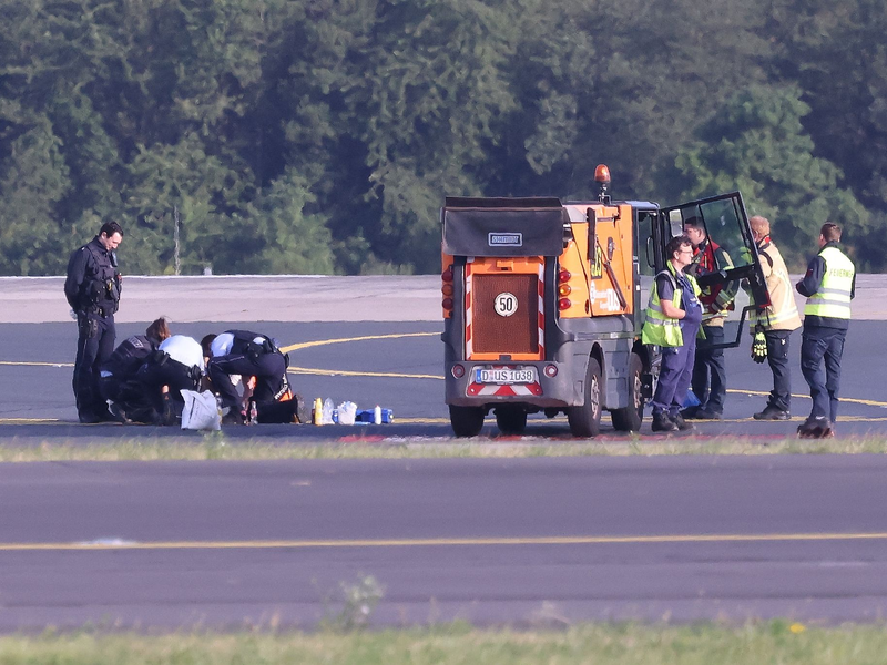 Sicherheitspersonal und Polizisten versuchen am Düsseldofer Flughafen, Aktivisten vom Asphalt auf dem Rollfeld zu lösen. - Foto: David Young/dpa