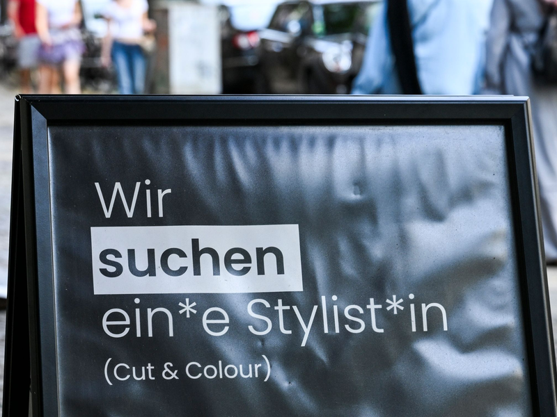 Auf einem Schild wird gendergerecht eine Stylistin beziehungsweise ein Stylist gesucht. - Foto: Jens Kalaene/dpa