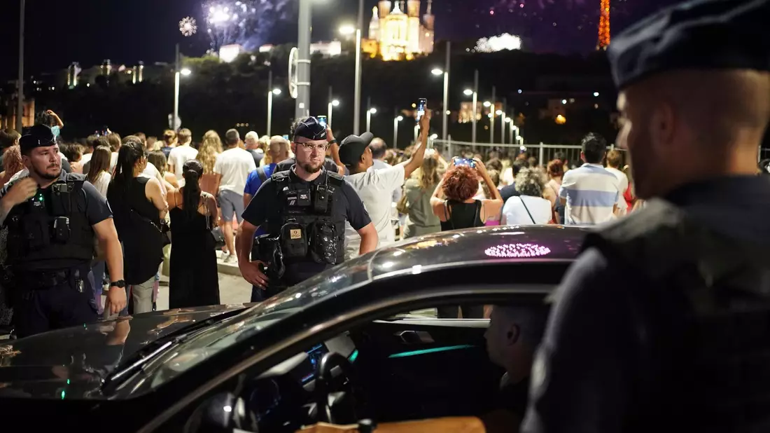 Polizisten kontrollieren einen Autofahrer in Lyon, während die Menschen ein Feuerwerk zum Tag der Bastille beobachten. - Bild: Laurent Cipriani/AP