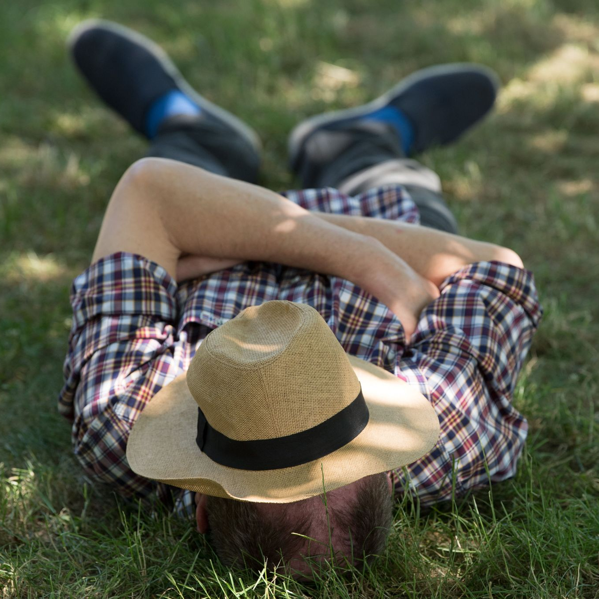 Ein Mann mit einem Sonnenhut auf dem Gesicht liegt auf einer Wiese im Schatten und ruht sich aus. - Foto: Sebastian Kahnert/zb/dpa