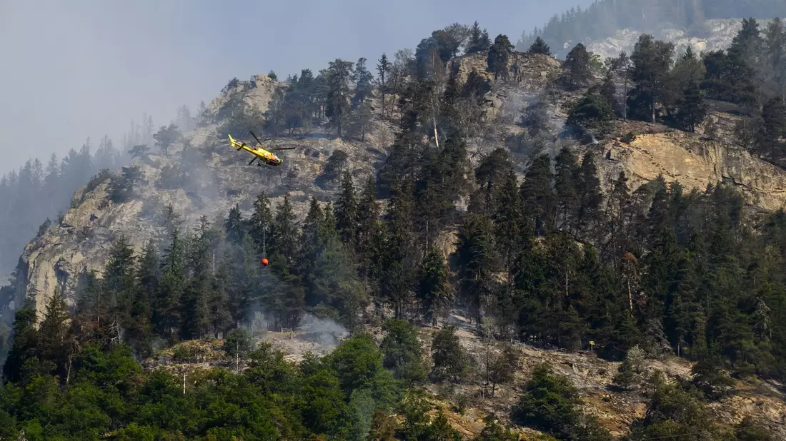 Ein Helikopter ist zur Bekämpfung des Waldbrandes nahe Bitsch im Einsatz. - Bild: Jean-Christophe Bott/KEYSTONE/dpa