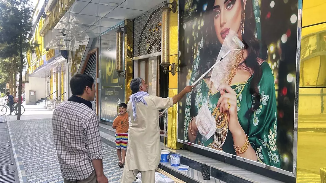 Ein Mitarbeiter eines Schönheitssalons übermalt nach der Machtübernahme der Taliban das Bild einer Frau in Kabul (Archivbild). Frauen haben in der afghanischen Hauptstadt gegen die Schließung der Salons protestiert. - Bild: -/Kyodo/dpa