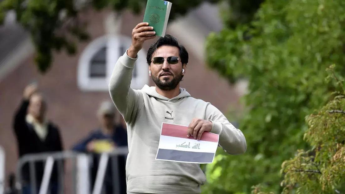 Ein Demonstrant hält eine Kopie des Korans hoch, die er mutmaßlich gemeinsam mit einer irakischen Fahne verbrennen will. - Bild: Oscar Olsson/TT NEWS AGENCY/AP/dpa