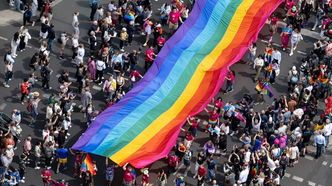 Menschen ziehen mit einer überdimensionalen Regenbogenfahne durch die Stadt. - Bild: Fabian Sommer/dpa