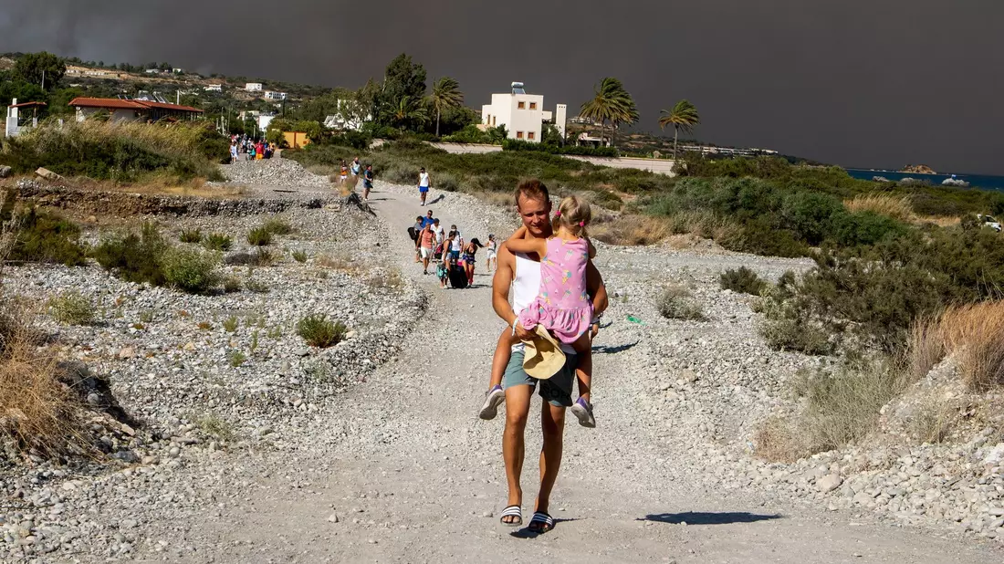 Menschen verlassen ein Waldbrandgebiet auf Rhodos. Auf der griechischen Insel wüten weiter mehrere Brände. - Bild: Lefteris Damianidis/InTime News/AP/dpa