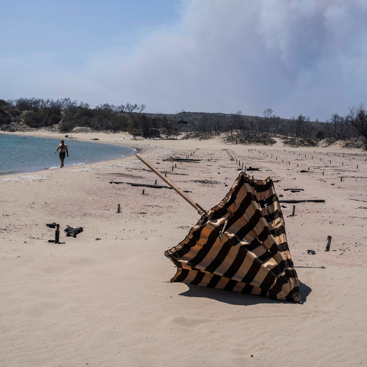 Verbrannte Sonnenliegen und Sonnenschirme an einem Strand auf Rhodos. - Foto: Petros Giannakouris/AP/dpa