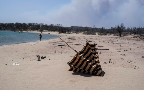 Verbrannte Sonnenliegen und Sonnenschirme an einem Strand auf der Ägäisinsel Rhodos. - Foto: Petros Giannakouris/AP/dpa