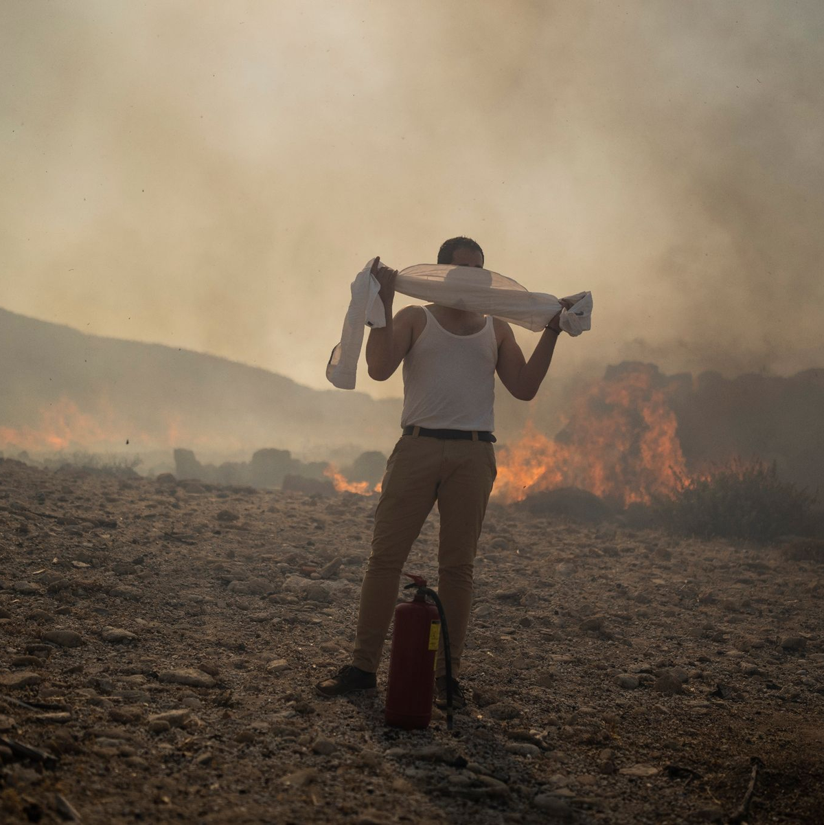Ein Mann schützt sich mit einem Handtuch vor dem Rauch, während er versucht, ein Feuer nahe des Badeortes Lindos zu löschen. - Foto: Petros Giannakouris/AP/dpa