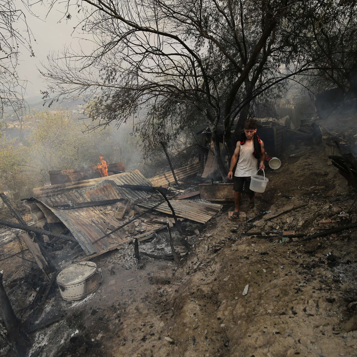 Ein Mann geht an einem Haus vorbei, das bei einem Waldbrand in der algerischen Provinz Bouira niedergebrannt ist. - Foto: XinHua/dpa