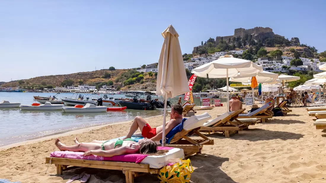 Touristen am Strand von Lindos auf Rhodos etwa 10 Kilometer von den Bränden im Südosten entfernt. - Bild: Christoph Reichwein/dpa