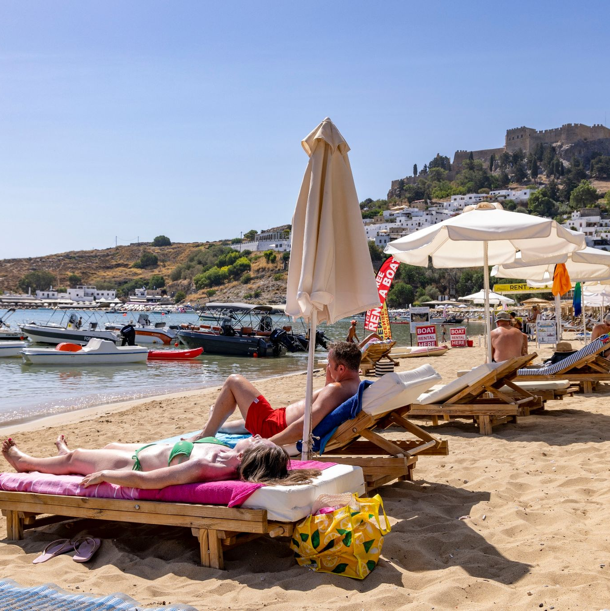 Touristen am Strand von Lindos auf Rhodos etwa 10 Kilometer von den Bränden im Südosten entfernt. - Foto: Christoph Reichwein/dpa