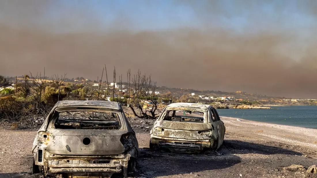 Ausgebrannte Autos am Strand von Kiotari. Im Hintergrund ist eine riesige Rauchwolke zu sehen. - Bild: Christoph Reichwein/dpa
