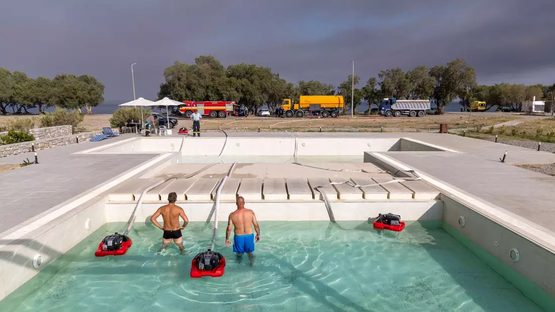 Feuerwehrleute pumpen aus einem Hotelpool in Gennadi das Wasser ab, um ihr Löschfahrzeug zu befüllen. - Bild: Christoph Reichwein/dpa