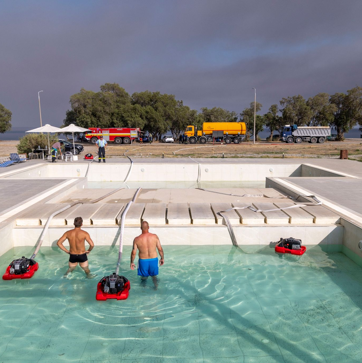 Feuerwehrleute pumpen aus einem Hotelpool in Gennadi das Wasser ab, um ihr Löschfahrzeug zu befüllen. - Foto: Christoph Reichwein/dpa