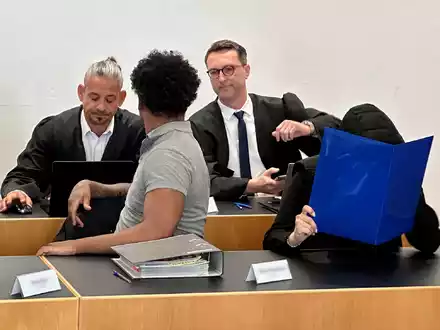 Eine ehemalige Justizvollzugsbeamtin (vorn r) und ein Häftling der Justizvollzugsanstalt Kaisheim (vorn l) sitzen auf der Anklagebank im Strafjustizzentrum Augsburg, im Hintergrund die Strafverteidiger. - Foto: Ulf Vogler/dpa