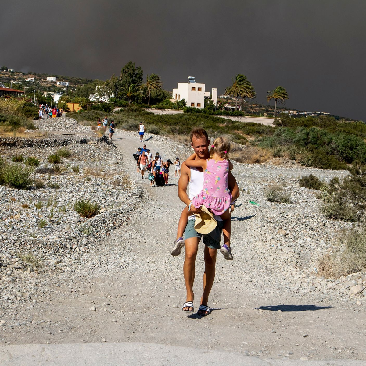 Ein Mann mit einem Kind auf dem Arm verlässt ein Waldbrandgebiet auf Rhodos. - Foto: Lefteris Damianidis/InTime News/AP/dpa