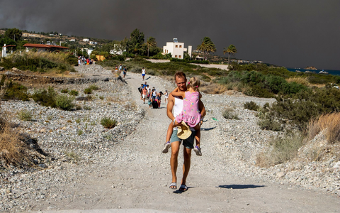 Ein Mann mit einem Kind auf dem Arm verlässt ein Waldbrandgebiet auf Rhodos. - Foto: Lefteris Damianidis/InTime News/AP/dpa