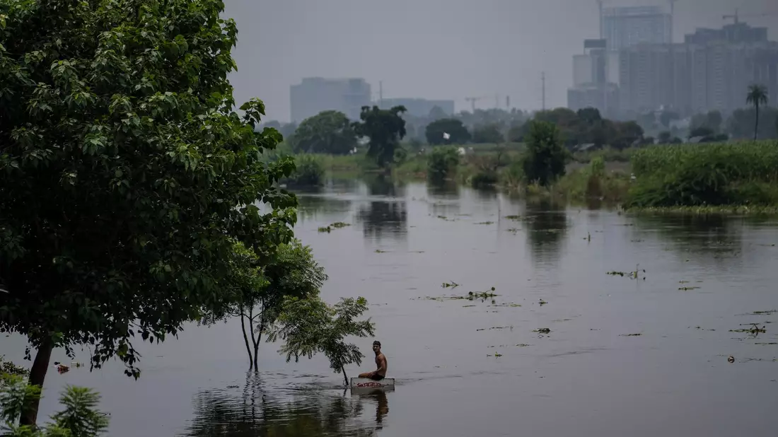 Ein Junge sitzt auf einem Schild in der Nähe einer Wohnkolonie, die vom Hochwasser des Flusses Hindon überschwemmt wurde. - Bild: Altaf Qadri/AP/dpa