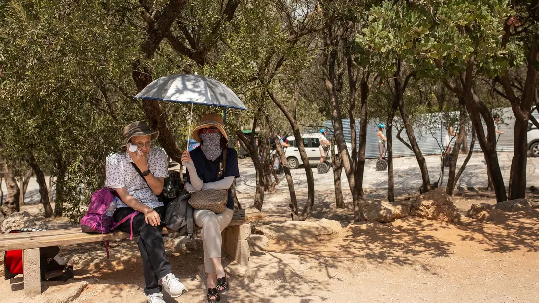 Touristen sitzen unter Bäumen am Eingang der Akropolis in Athen. - Bild: Socrates Baltagiannis/dpa