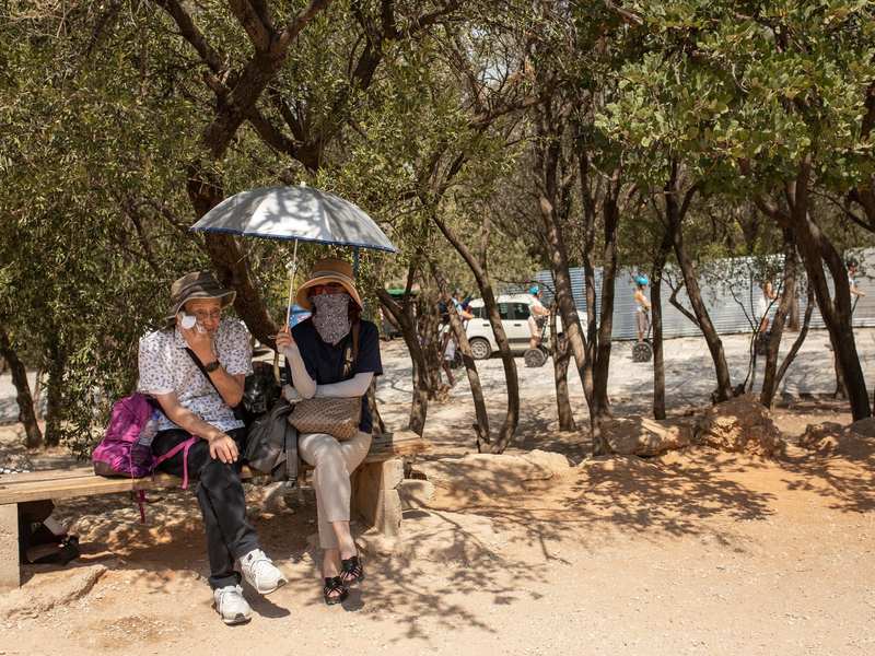 Touristen unter Bäumen am Eingang der Akropolis im Hitzesommer 2023. - Foto: Socrates Baltagiannis/dpa