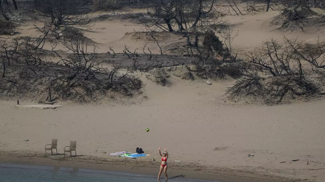 Hinten die verbrannte Vegetation, vor das Mittelmeer. Eine Frau spielt mit einem Ball am Strand bei Gennadi auf Rhodos. - Bild: Petros Giannakouris/AP